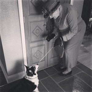 Black and white photo of a woman pretending to be the queen pointing a sword toward a black and white corgi