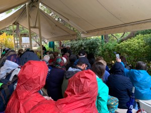 Large group of people under an awning in a garden listening to a pastor