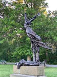 Bronze modern statue of an angel with a trumpet taking flight over a fallen soldier
