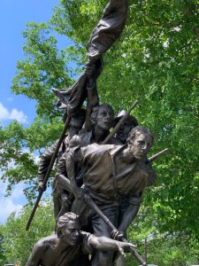 Bronze statue of 5 men heading into battle, one holding a flag, three holding rifles and one kneeling and pointing.