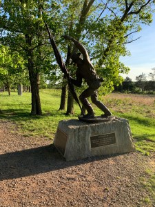 Bronze statue of a man holding a flag in his right hand and using his left hand to motion others to come on